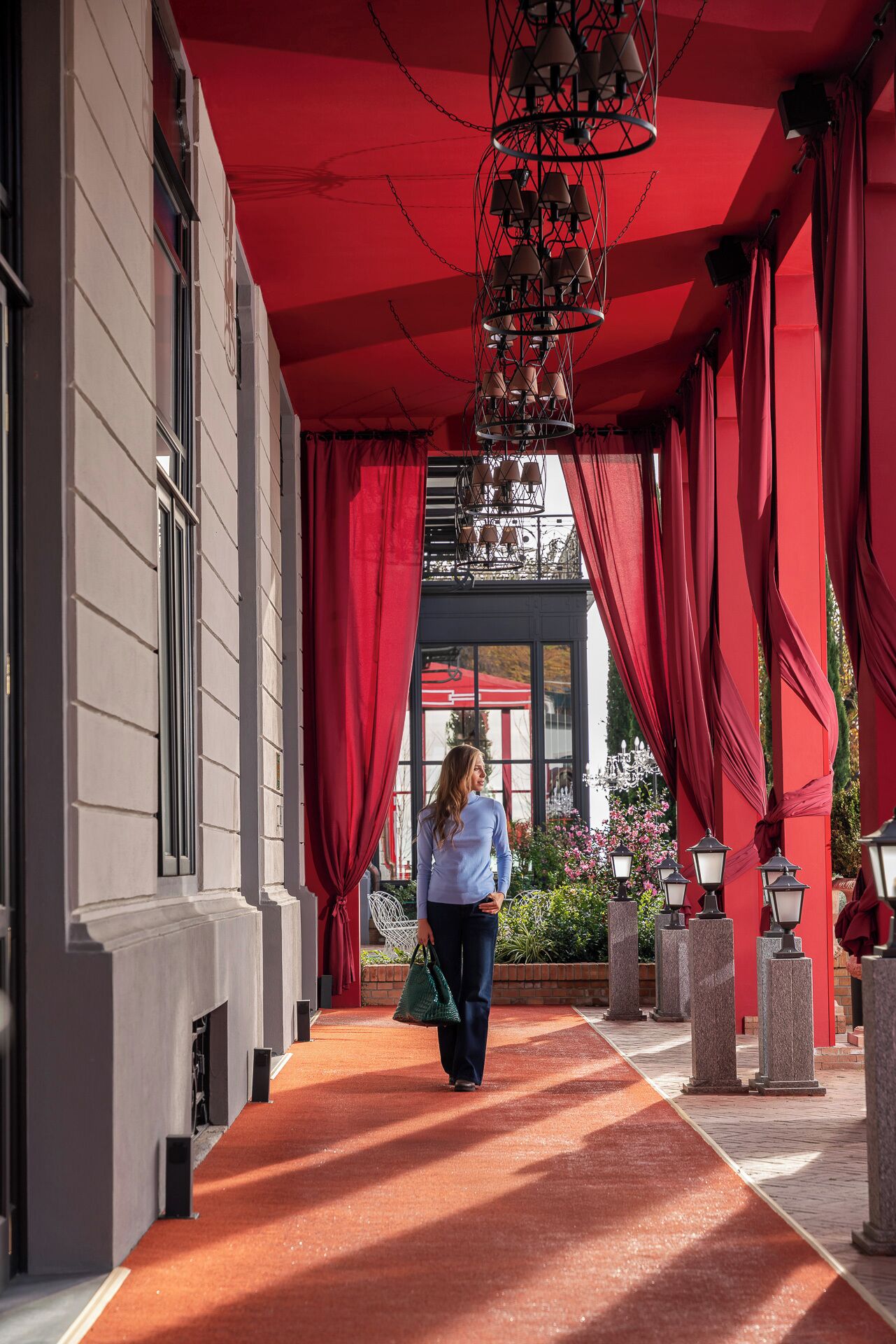 A corridor with red drapes, a chandelier, and a red carpet leading to a building entrance.