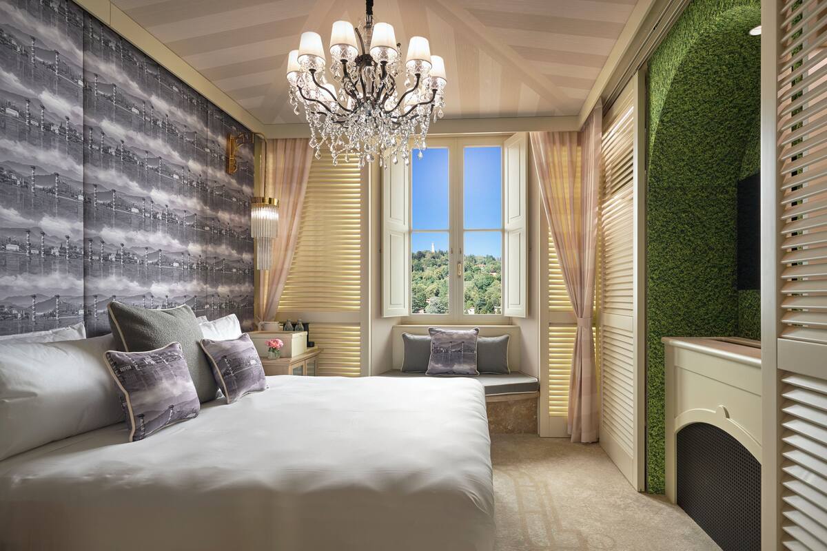 Un dormitorio con una cama grande, un candelabro, una ventana con vista a follaje y una chimenea.