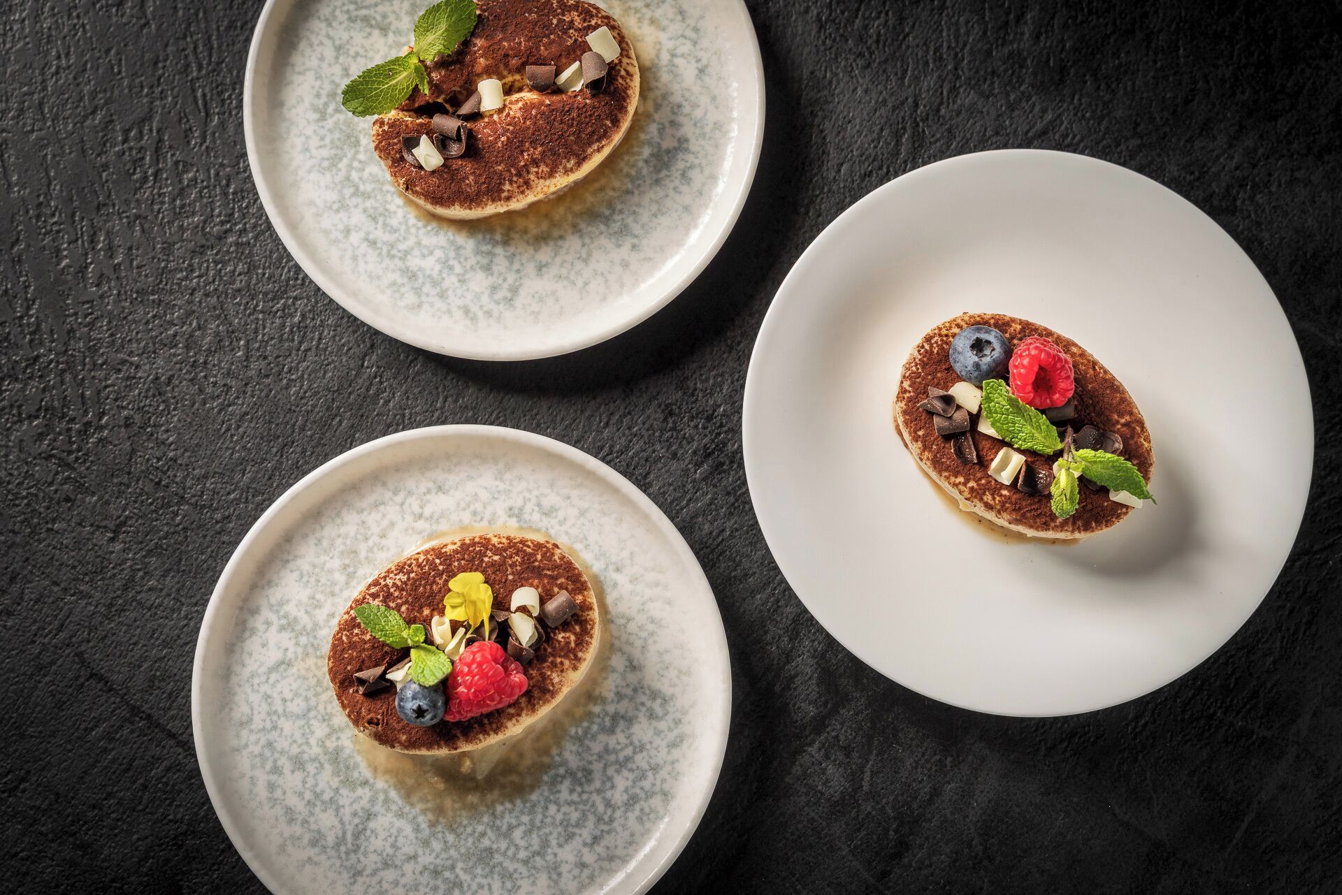Tres platos de postres sobre una superficie oscura.