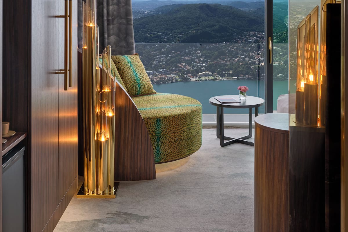 Una habitación moderna con un sofá curvo, una pequeña mesa redonda y vistas a un lago y montañas.