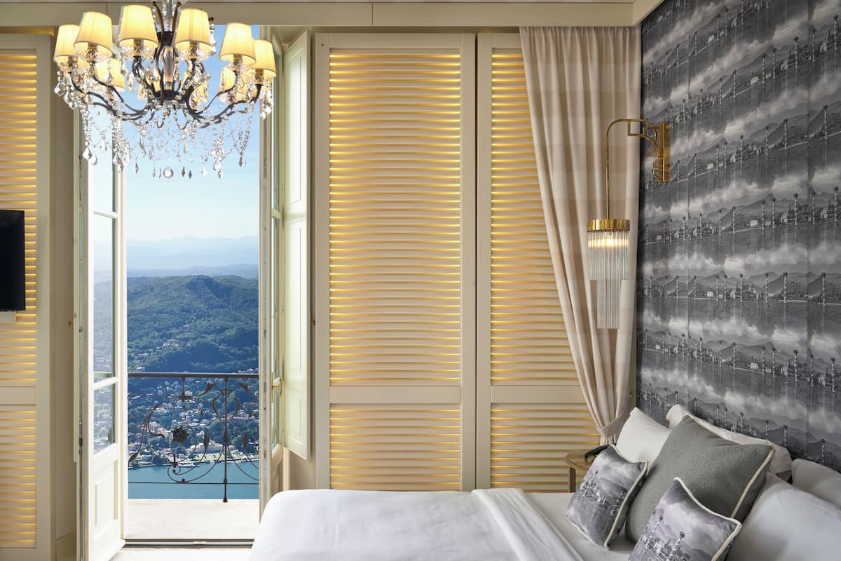 Un dormitorio con una cama grande, una araña de techo, vistas a un paisaje urbano y un balcón.