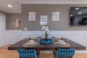 Uma sala de jantar com uma mesa de madeira escura, cadeiras estofadas em branco e azul, e um arranjo de flores brancas.