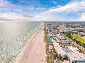 Vue aérienne d’une zone côtière avec une plage, des hôtels et un port de plaisance.