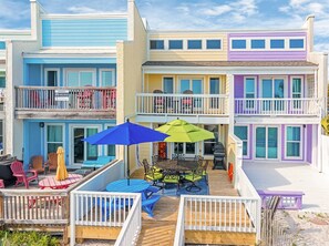 Une propriété colorée située en bord de mer, dotée de plusieurs balcons, d’un espace salon extérieur et d’une terrasse en bois.