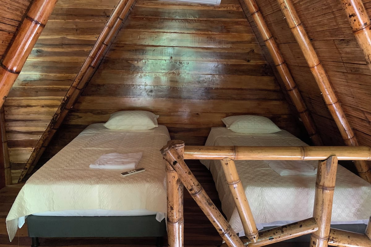A room with a sloped ceiling and wooden beams, featuring two beds with pillows and a remote control on one bed.