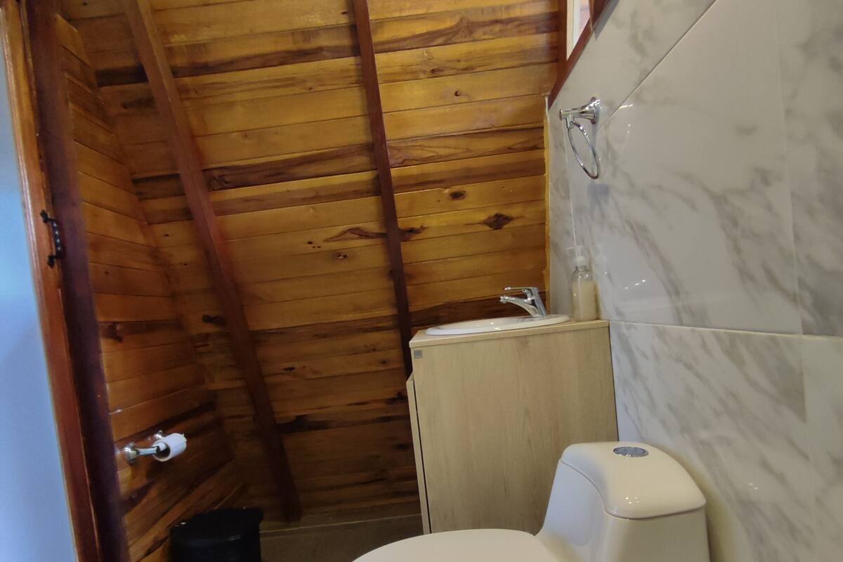 A small, compact bathroom with wooden walls, a white toilet, and a marble-tiled shower area.