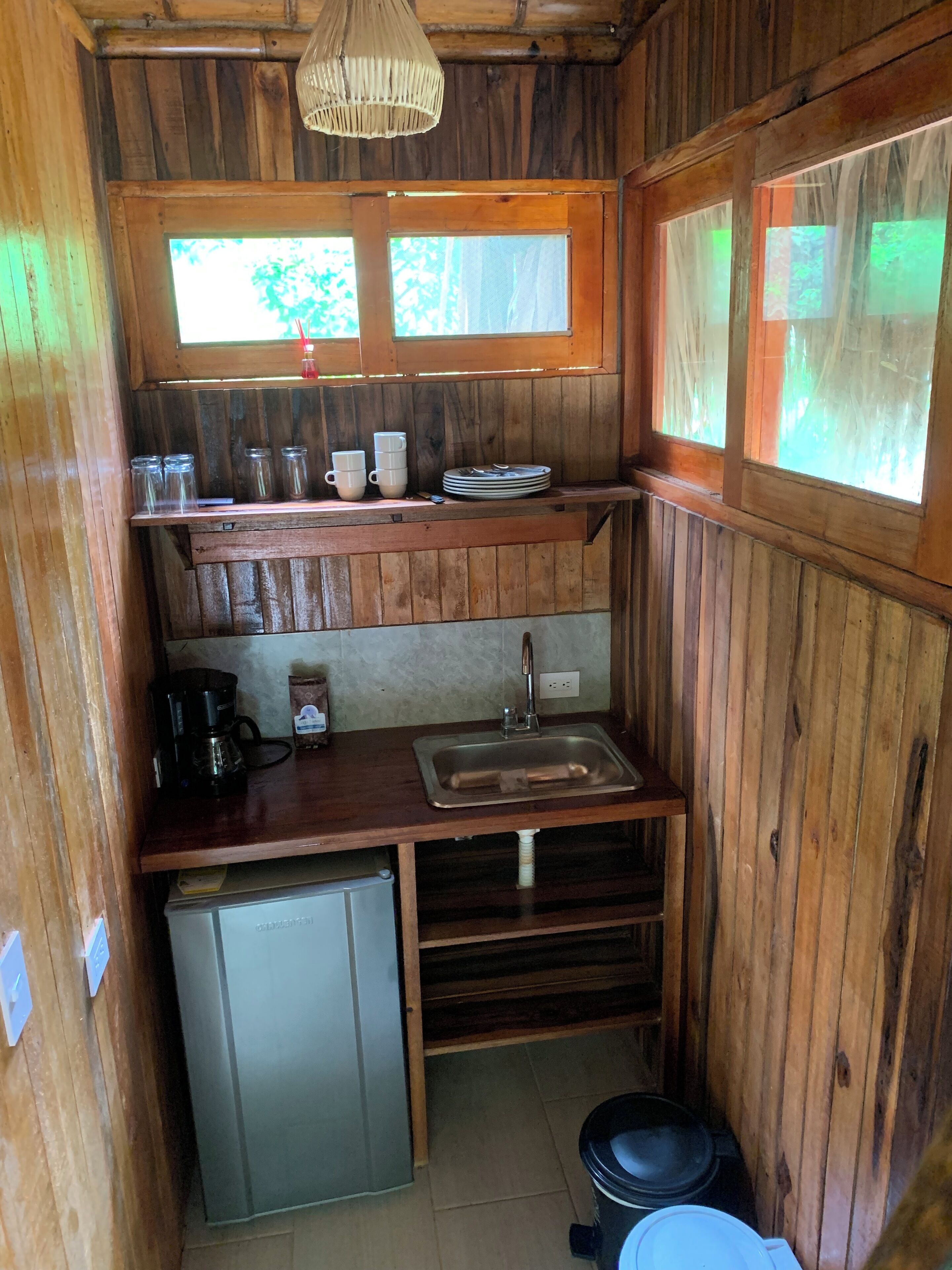A compact wooden kitchen with a sink, a coffee maker, and a small refrigerator.