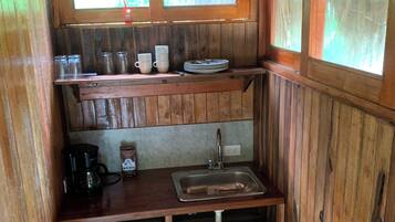 A compact wooden kitchen with a sink, a coffee maker, and a small refrigerator.