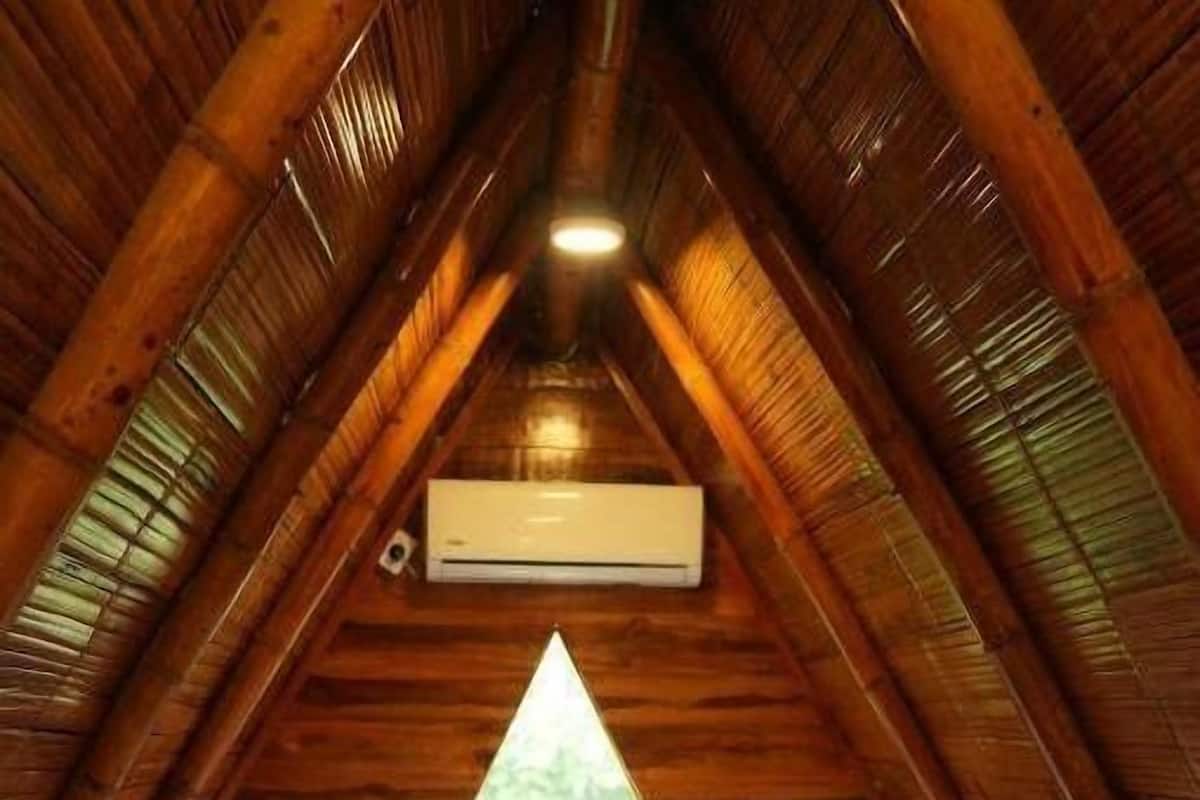 A small, cozy attic bedroom with a wooden interior, a single bed, a window, and an air conditioning unit.