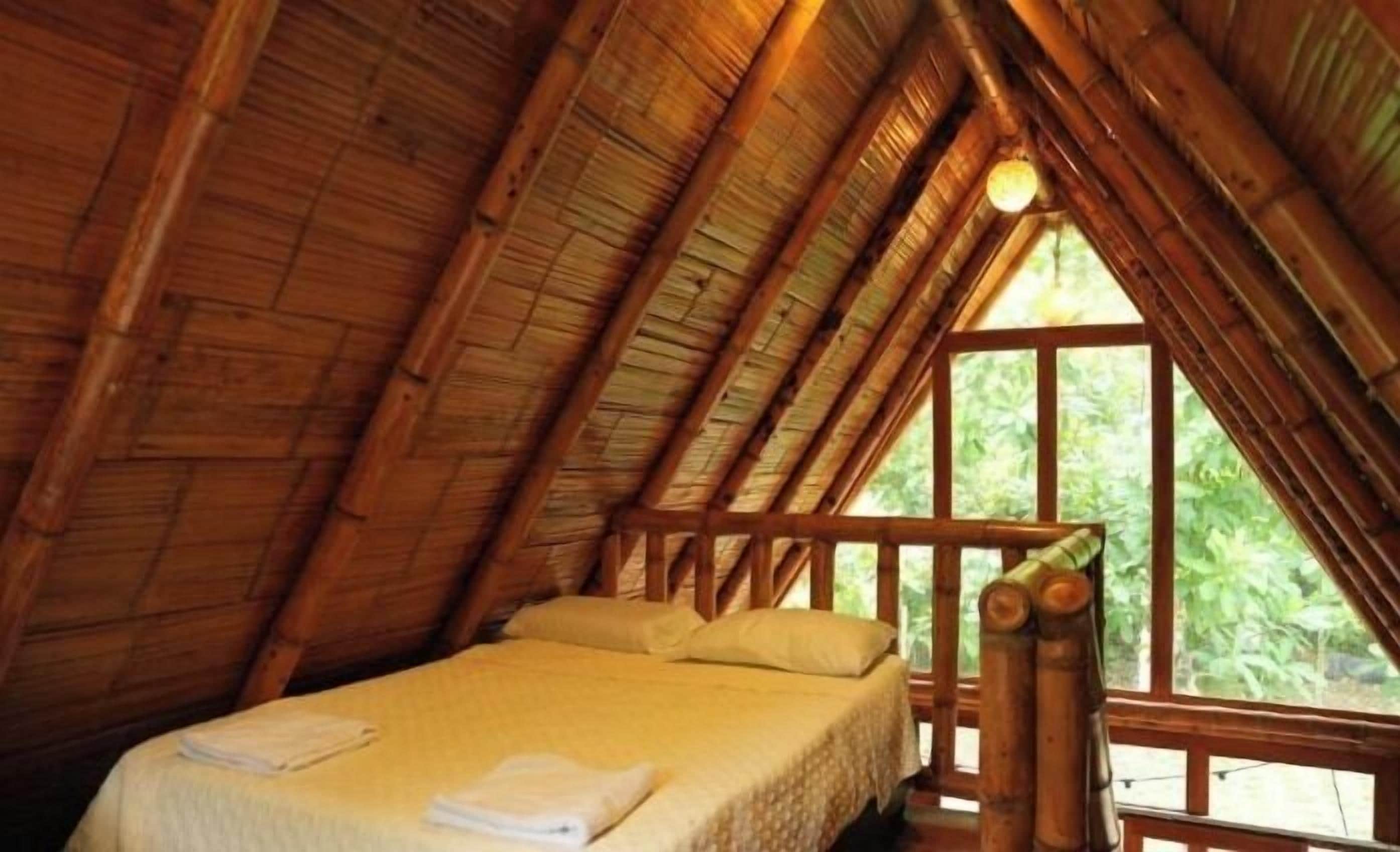 A cozy, wooden-roofed room with a bed and a window overlooking greenery.