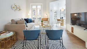 A modern living room with a sofa, two blue chairs, a coffee table, a TV, and a dining area with a table and chairs. - Getaria by FeelFree Rentals (San Sebastian)