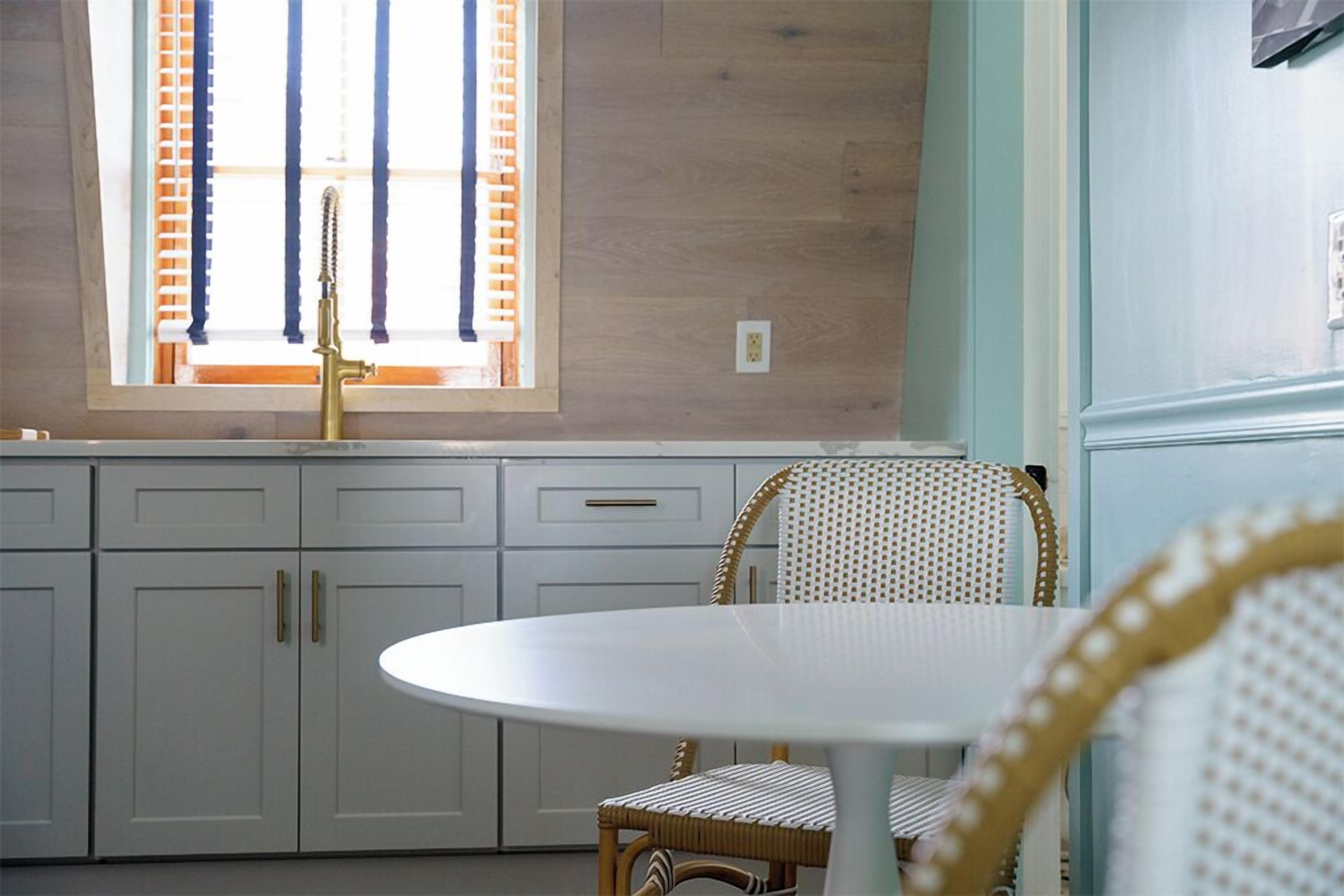 A kitchen with white cabinets, a round white table, and a wicker chair.