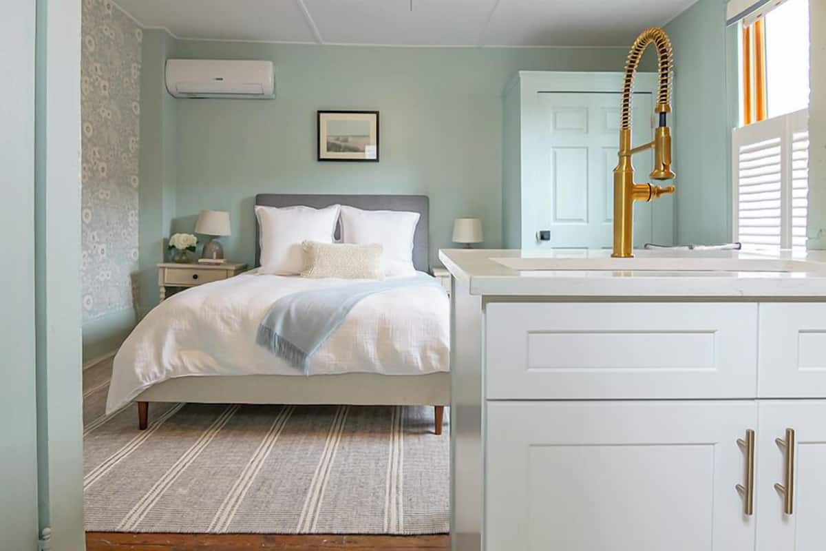 A bedroom with a bed, nightstands, a dresser, a vanity with a sink, and a window with blinds.