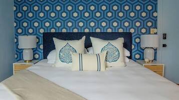 Ein Bett mit dunklem Kopfteil, zwei Nachttischlampen und dekorative Kissen mit geometrischem Muster.