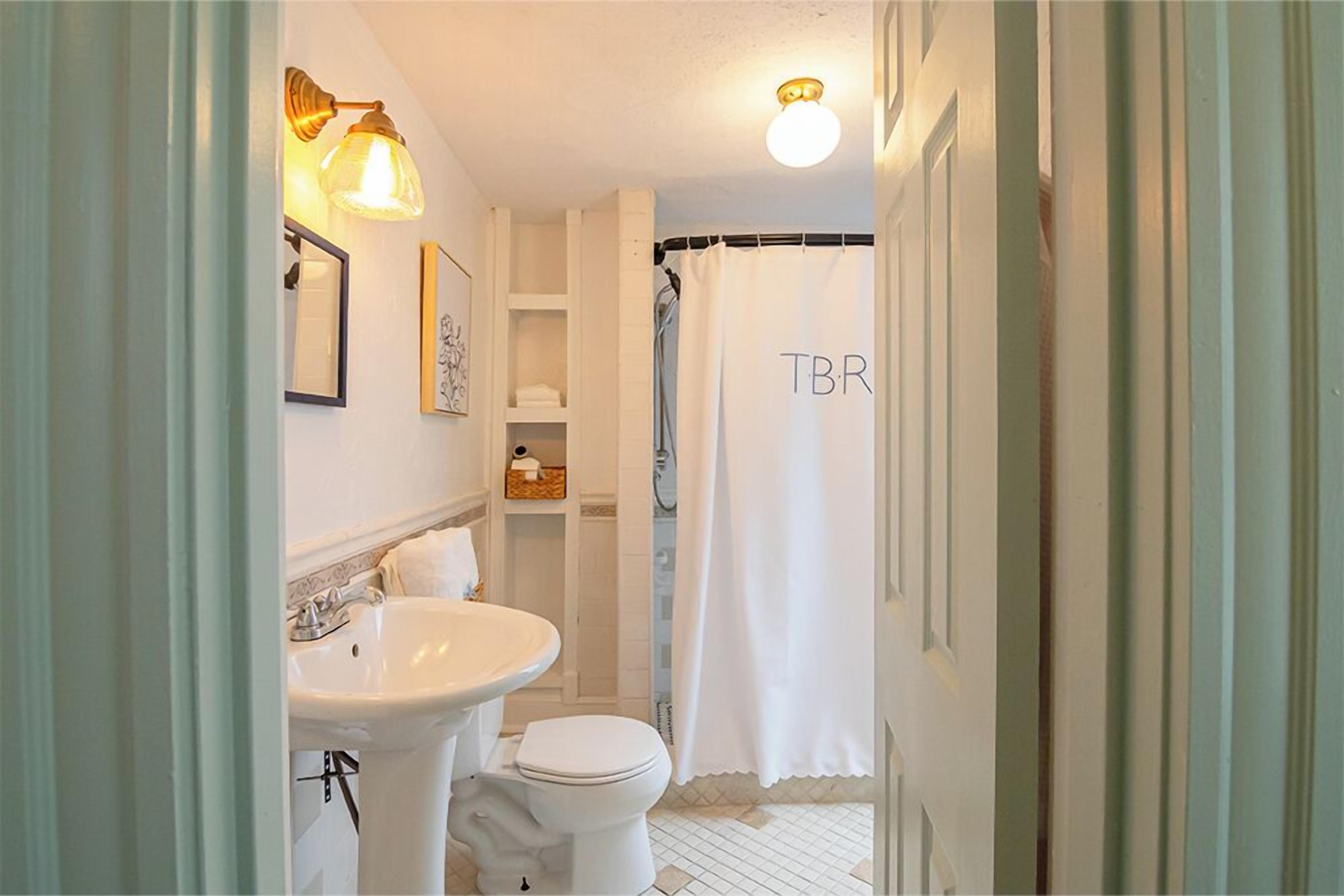 A bathroom with a white sink, toilet, and shower curtain with "TBR" on it.