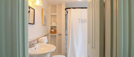 A bathroom with a white sink, toilet, and shower curtain with "TBR" on it.