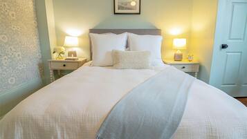A neatly made bed with white linens and pillows, two bedside lamps, and a framed picture on the wall.
