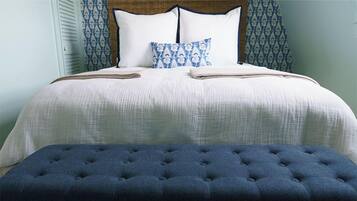 A neatly made bed with a blue upholstered bench in front, a patterned pillow, and a headboard with a wooden panel.
