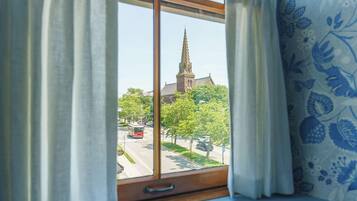 A window with curtains, a view of a church spire, and a tram in the distance.