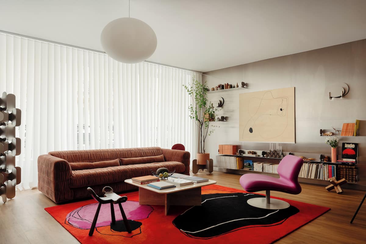 Un salon moderne avec un canapé marron, une table basse, un tapis rouge et un fauteuil rose.