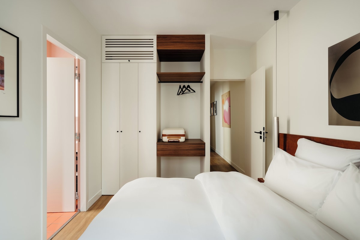 A hotel room with a bed, a wardrobe, a hanging coat rack, and a painting on the wall.