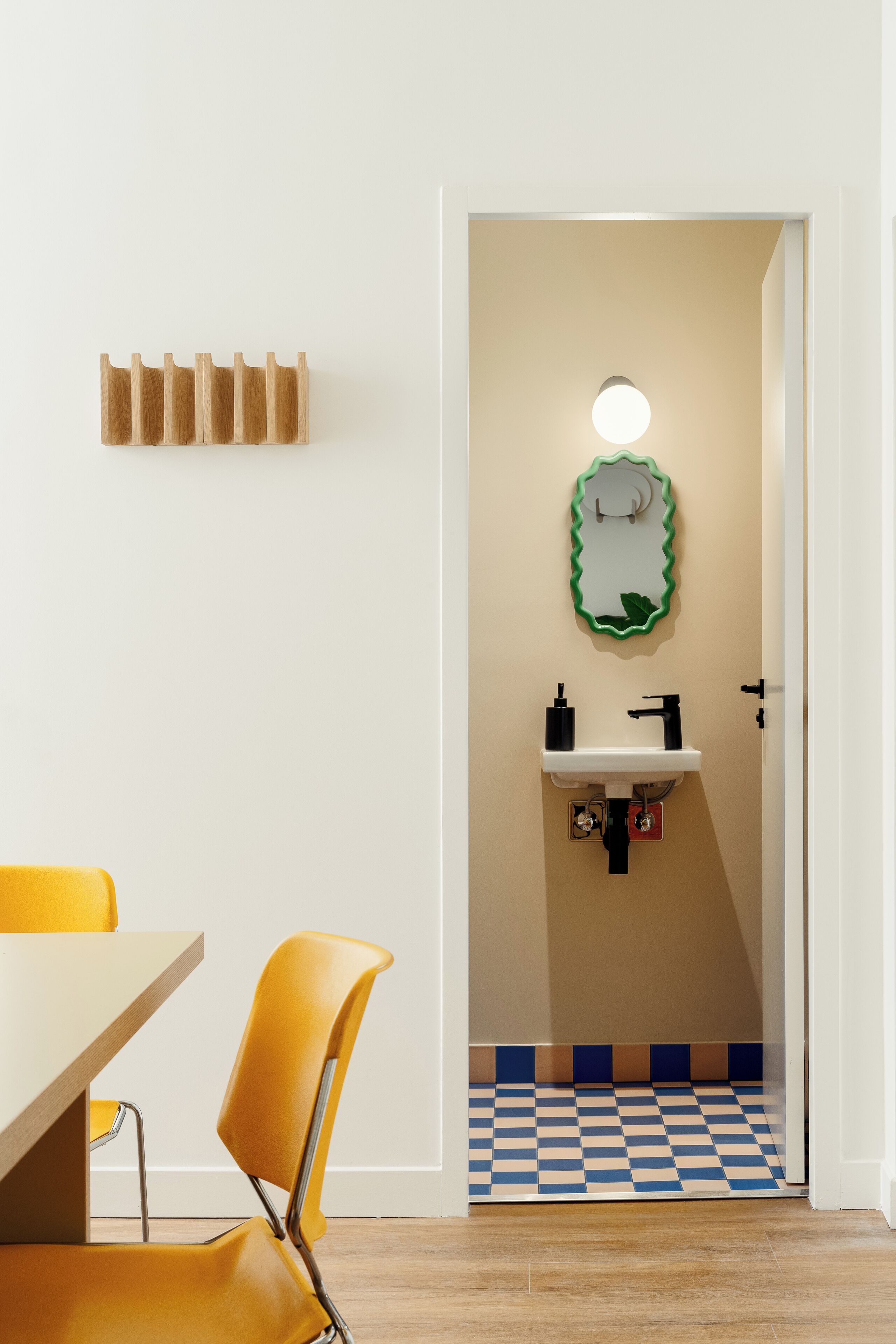A room with a checkered floor, a yellow chair, a white table, a sink with a green mirror, and a light fixture.