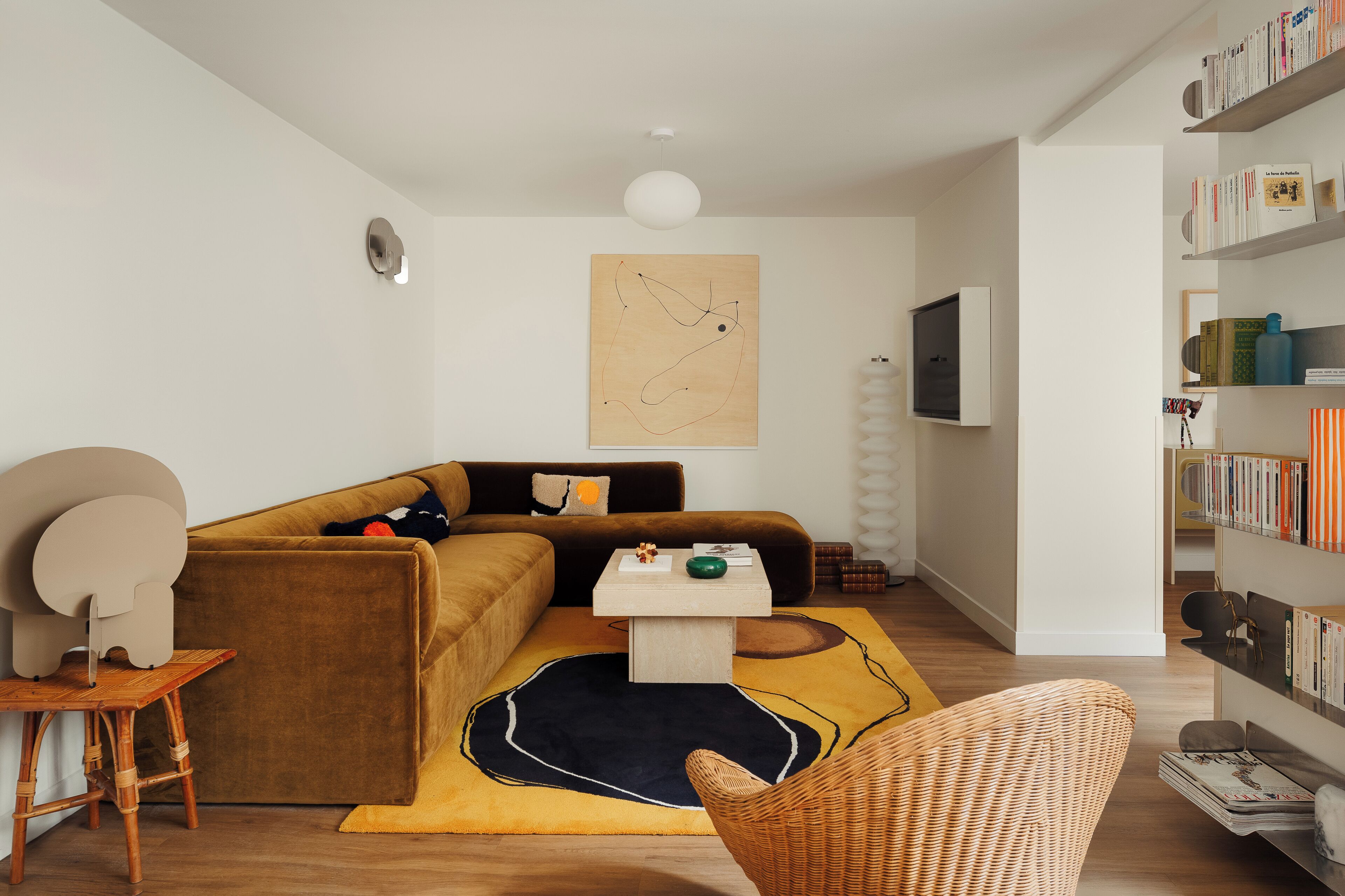 A modern living room with a brown sofa, a coffee table, a bookshelf, and a large abstract painting on the wall.