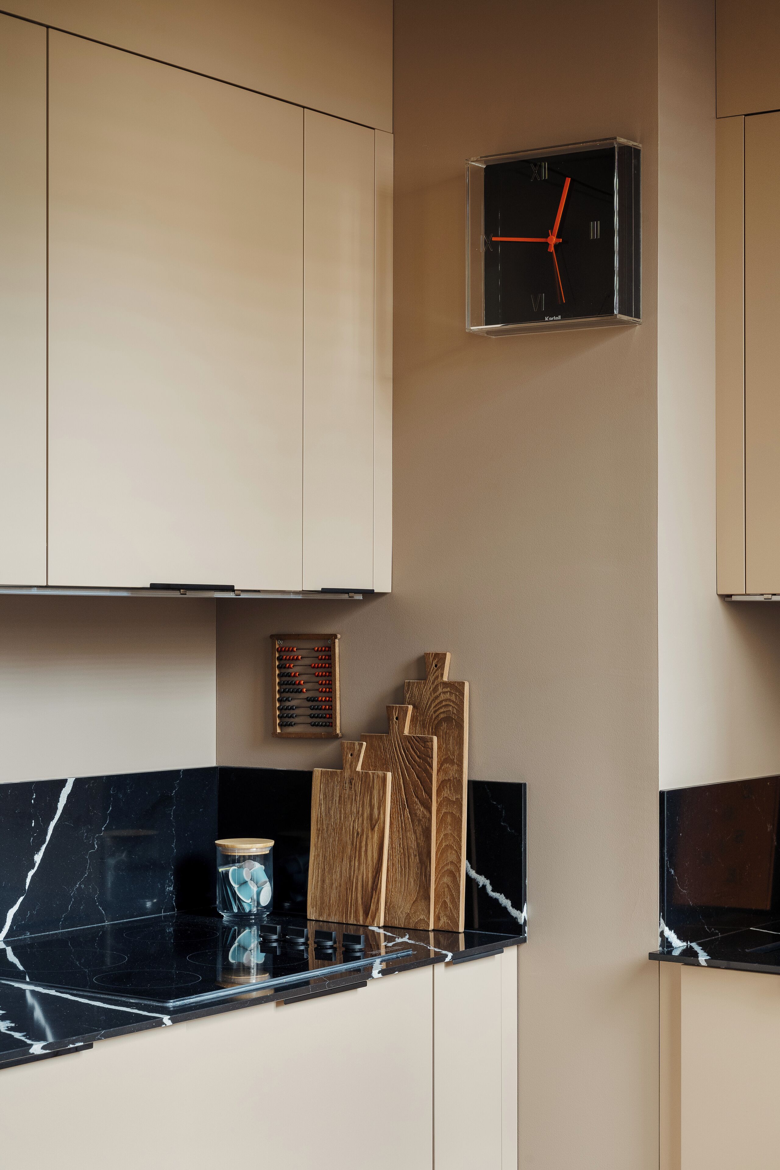 A kitchen with a black clock, wooden cutting boards, and a marble countertop.