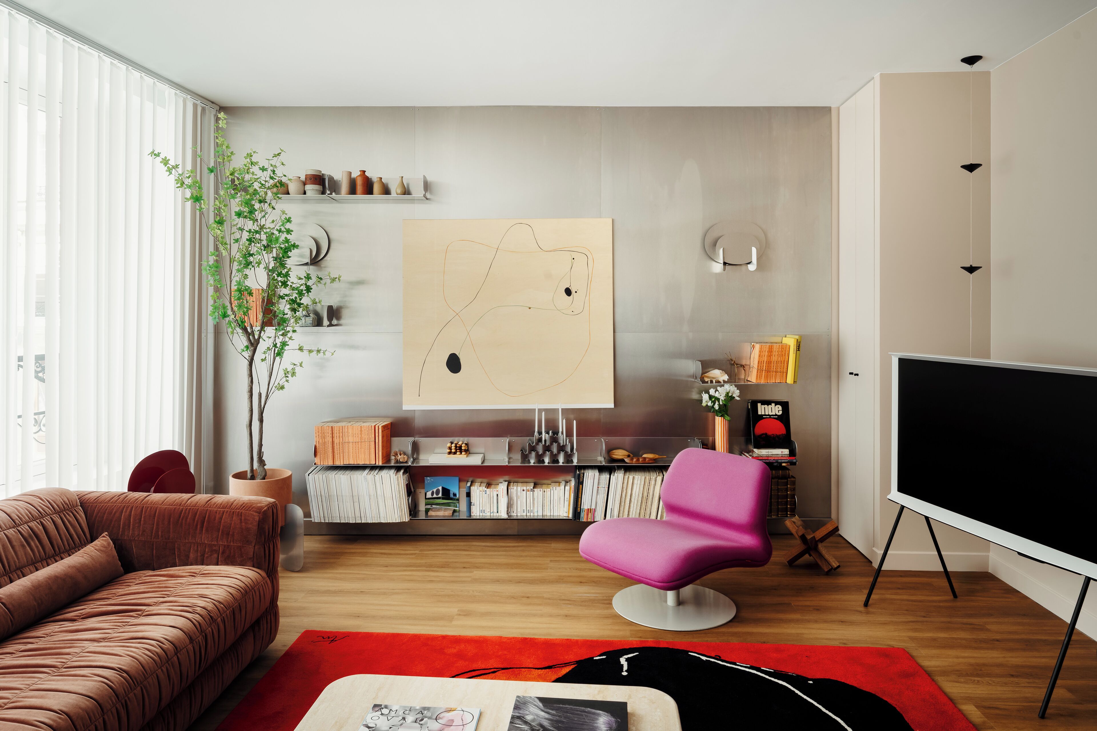 Un salon moderne avec un canapé, un fauteuil rose, un téléviseur à écran plat, une bibliothèque et un grand tableau abstrait.