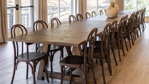 A large dining room with a long wooden table and matching chairs, large windows with curtains, and hanging pendant lights. - Spacious Mtn Retreat on 40+ Acres (Horse Shoe)
