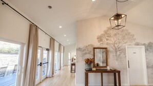 A spacious hallway with a wooden floor, large windows with curtains, a console table with a vase, and a wall mural. - Spacious Mtn Retreat on 40+ Acres (Horse Shoe)