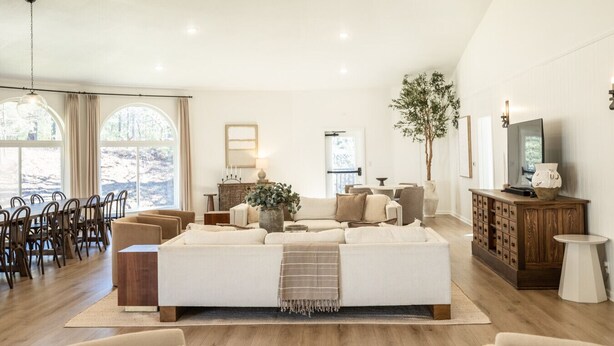 A spacious living room with a large sofa, dining area with chairs, a television, and a wooden cabinet. - Spacious Mtn Retreat on 40+ Acres (Horse Shoe)