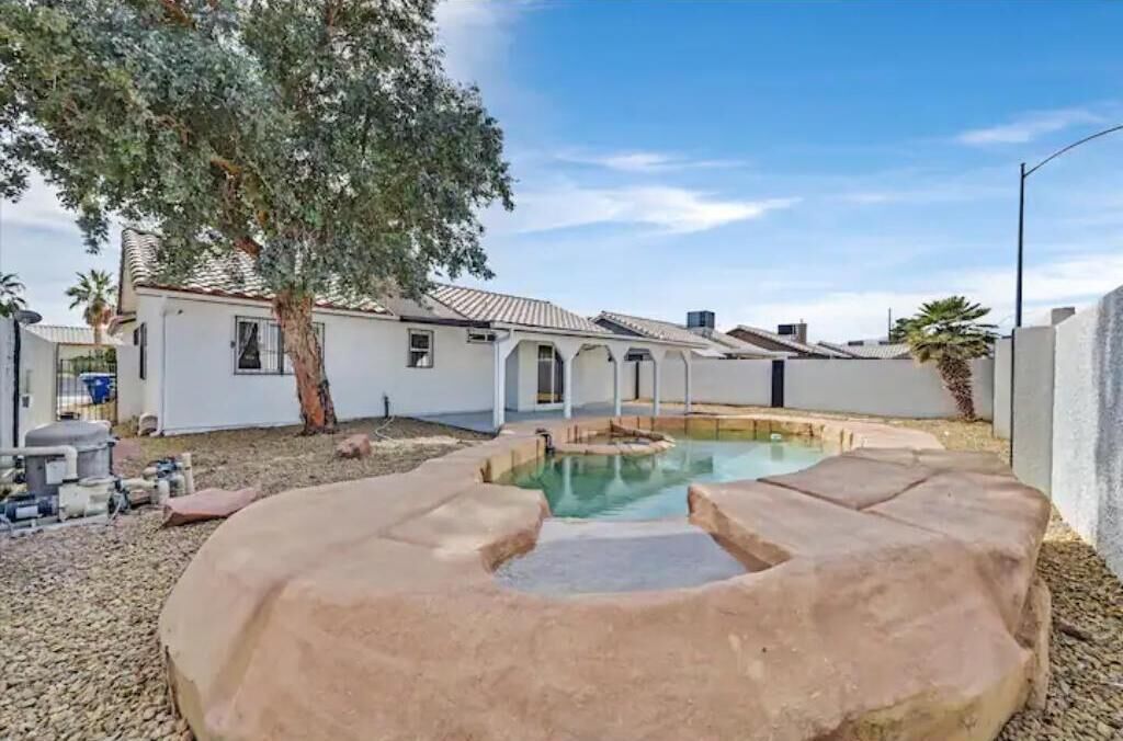A backyard with a swimming pool, a tree, and a house.