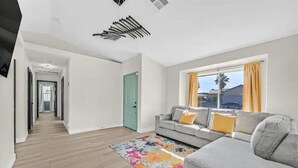A modern living room with a grey sofa, colorful rug, and a window with curtains. - Vegas Jackpot: With Pool & Spa (North Las Vegas)
