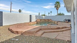 A swimming pool with a stone border and a white wall in the background. - Vegas Jackpot: With Pool & Spa (North Las Vegas)