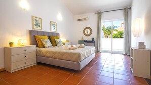 Un dormitorio con cama, mesitas de noche, un escritorio, aire acondicionado y vistas al exterior.