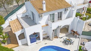Una villa moderna con piscina, mobiliario de exterior y un porche cubierto.