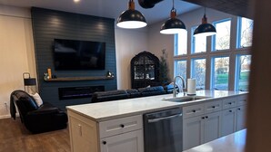 A modern kitchen with a large island, built-in appliances, and a dining area with a black leather sofa. - Big Wolf Barn: Where Big Groups Have Big Fun, Lakegfront in Jackson, MI. (Jackson)