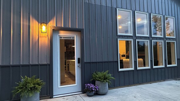 A modern building with a metal exterior, a door with a glass panel, and multiple windows. There are two potted plants in front. - Big Wolf Barn: Where Big Groups Have Big Fun, Lakegfront in Jackson, MI. (Jackson)