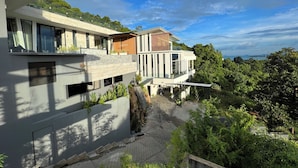 A modern multi-story building with large windows, a rooftop terrace, and lush greenery surrounding it. - Magic Suites (Koh Samui)