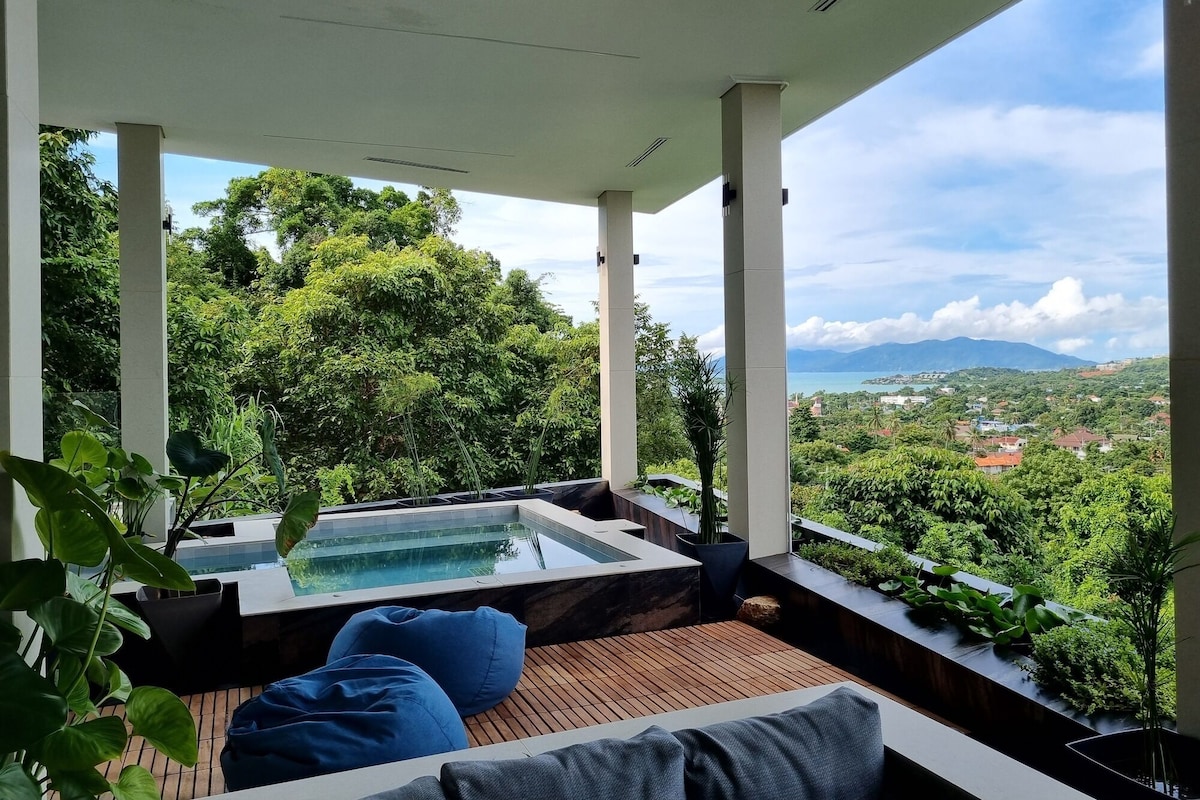 A covered outdoor area with a hot tub, wooden flooring, and seating.
