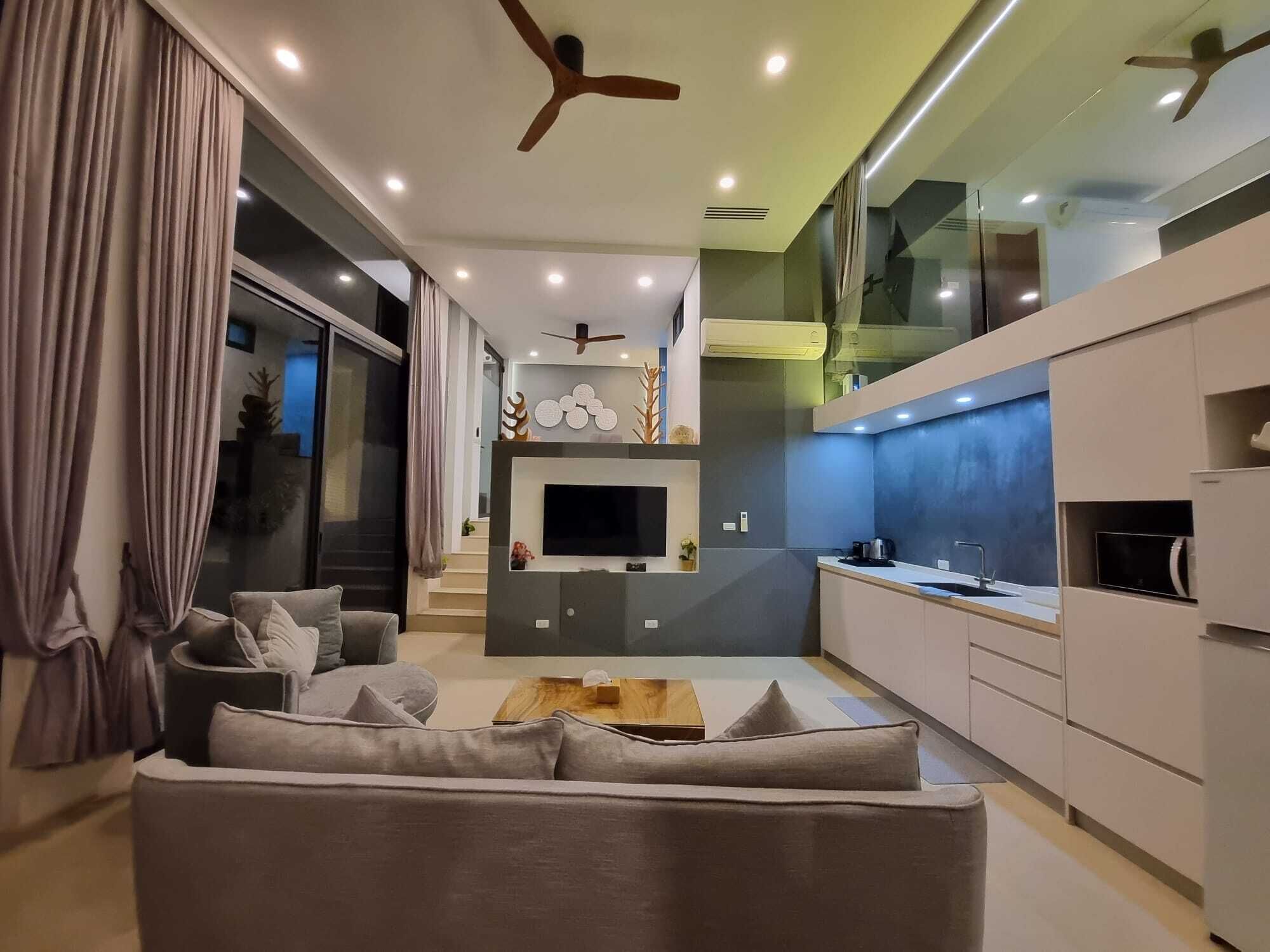 A modern living room with a sofa, TV, and kitchen area with cabinets and a countertop.