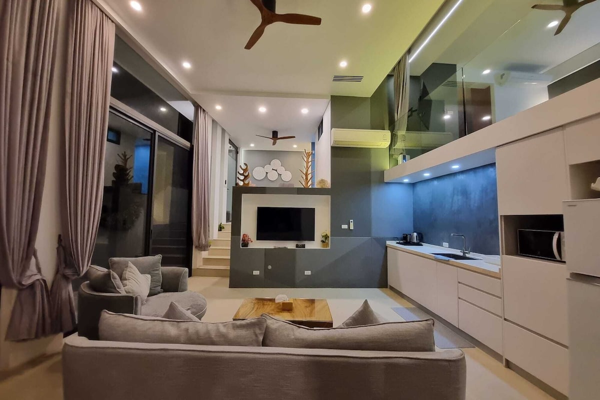 A modern living room with a sofa, TV, and kitchen area with cabinets and a countertop.