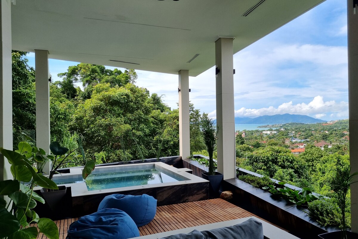 Un área de lounge al aire libre moderna con terraza de madera, cojines azules y grises, y un jacuzzi.