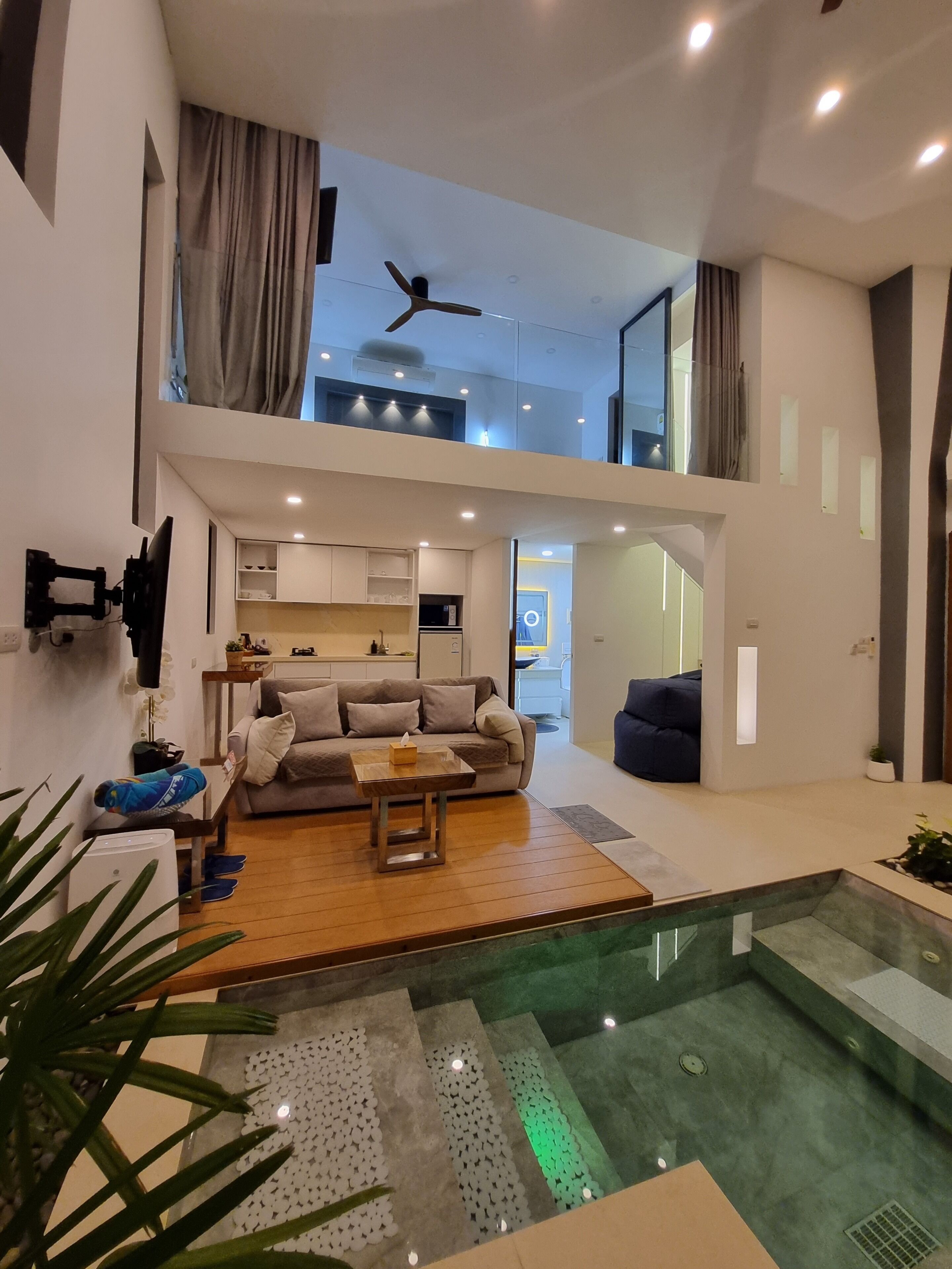 A modern living room with a sofa, coffee table, and a small table with a tissue box. There is a staircase leading to an upper level with a ceiling fan.