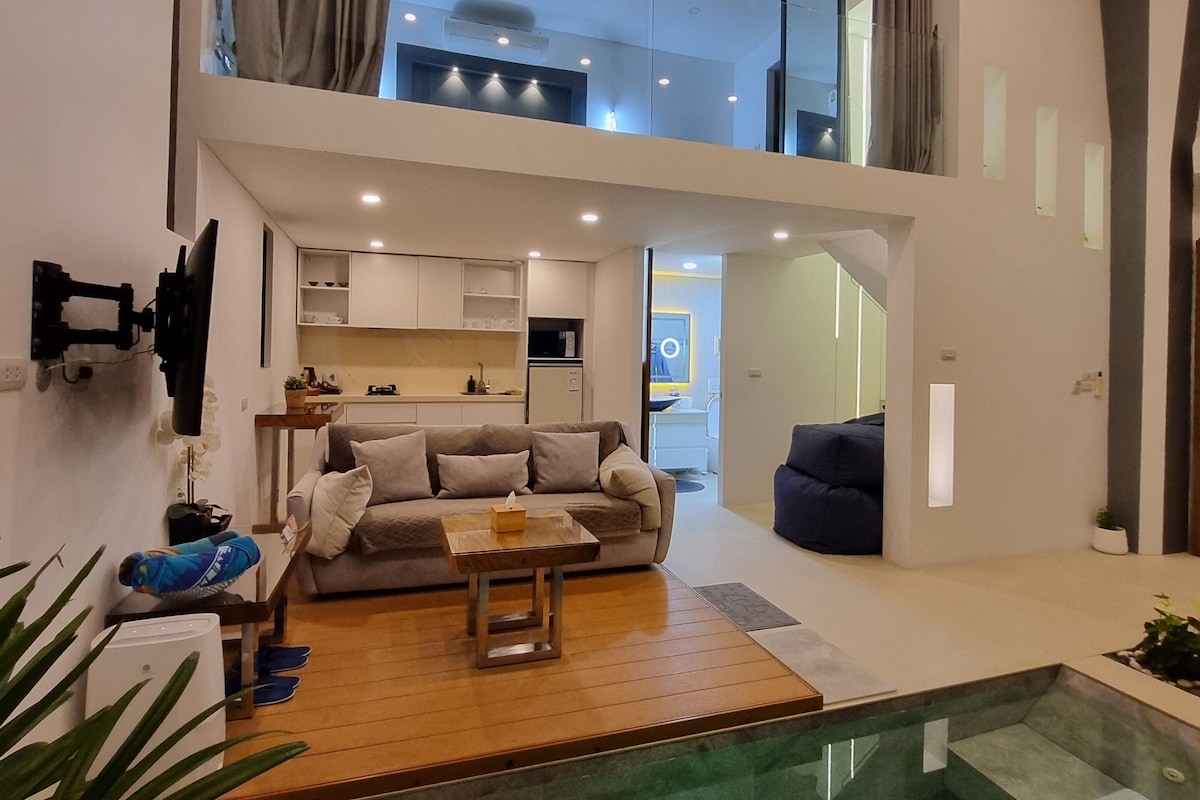 A modern living room with a sofa, coffee table, and a small table with a tissue box. There is a staircase leading to an upper level with a ceiling fan.