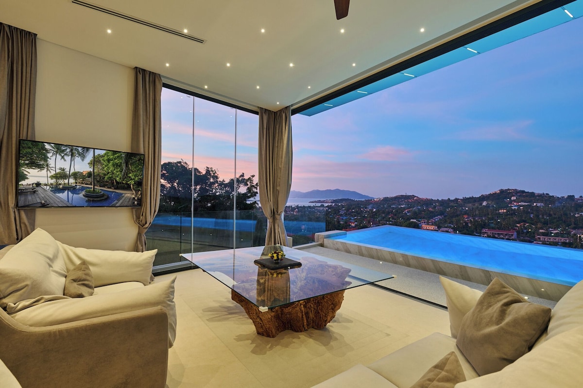 A modern living room with a glass coffee table, beige sofas, and a large TV.
