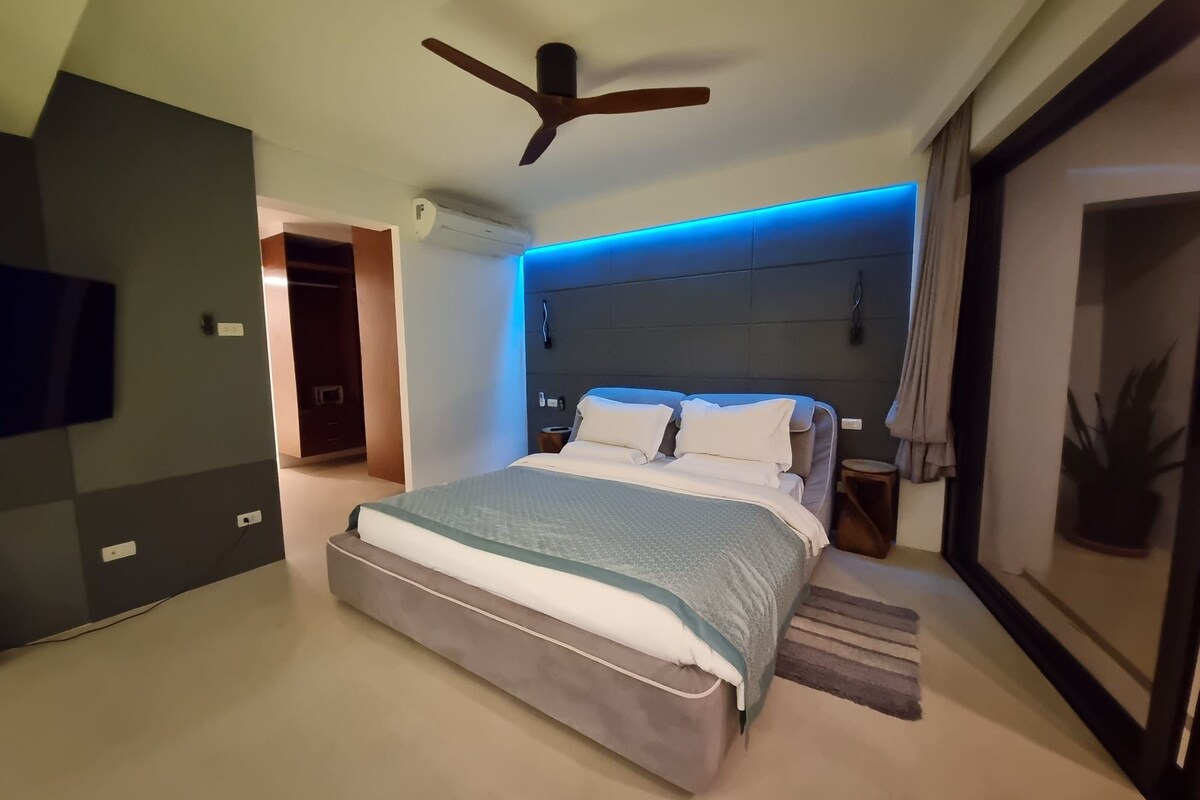 Un dormitorio moderno con una cama, ventilador de techo, equipo de aire acondicionado y televisor montado en la pared.