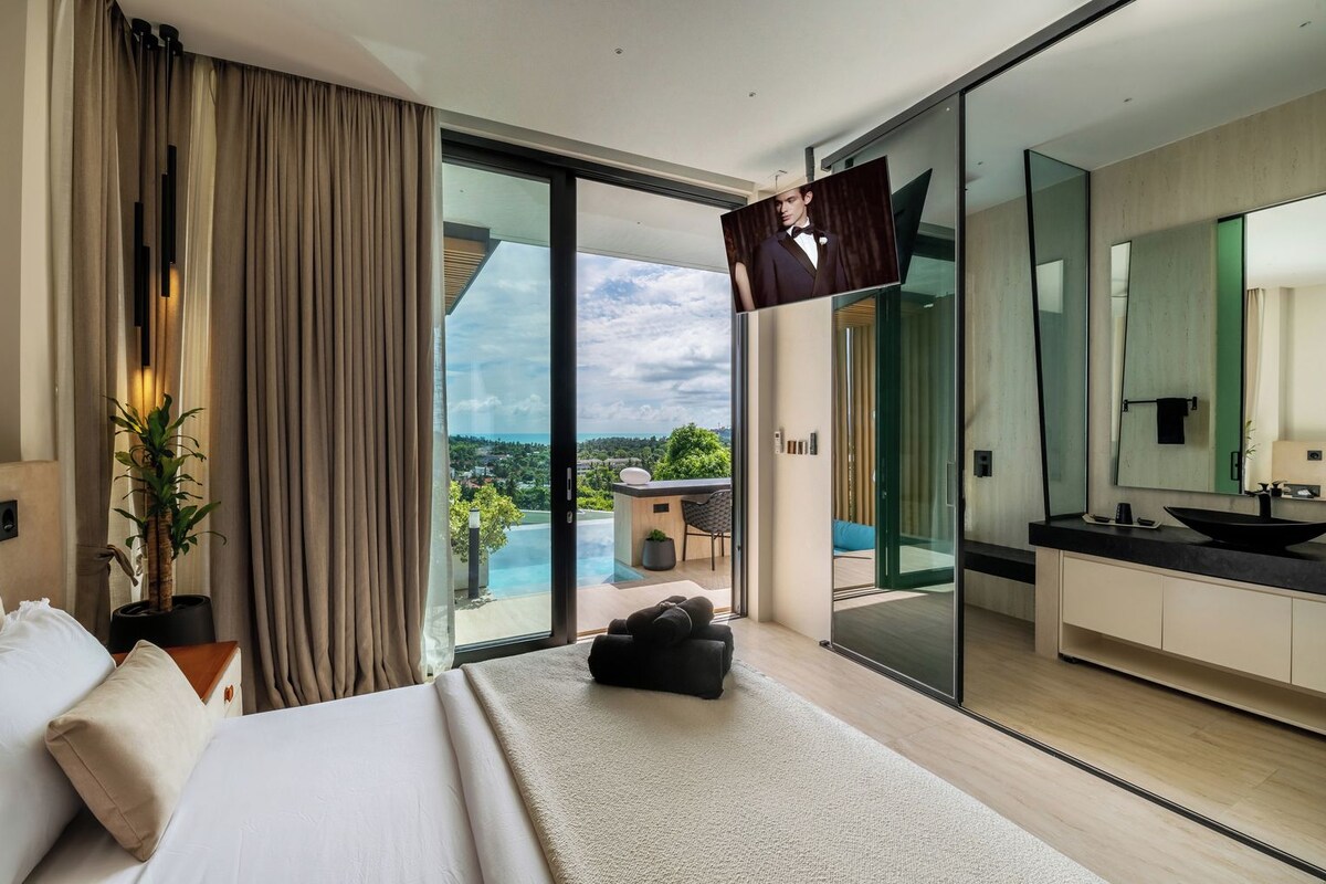 Una habitación de hotel moderna con una cama grande, vista a una piscina y paisaje, un baño con un espejo amplio y una puerta corrediza de vidrio.