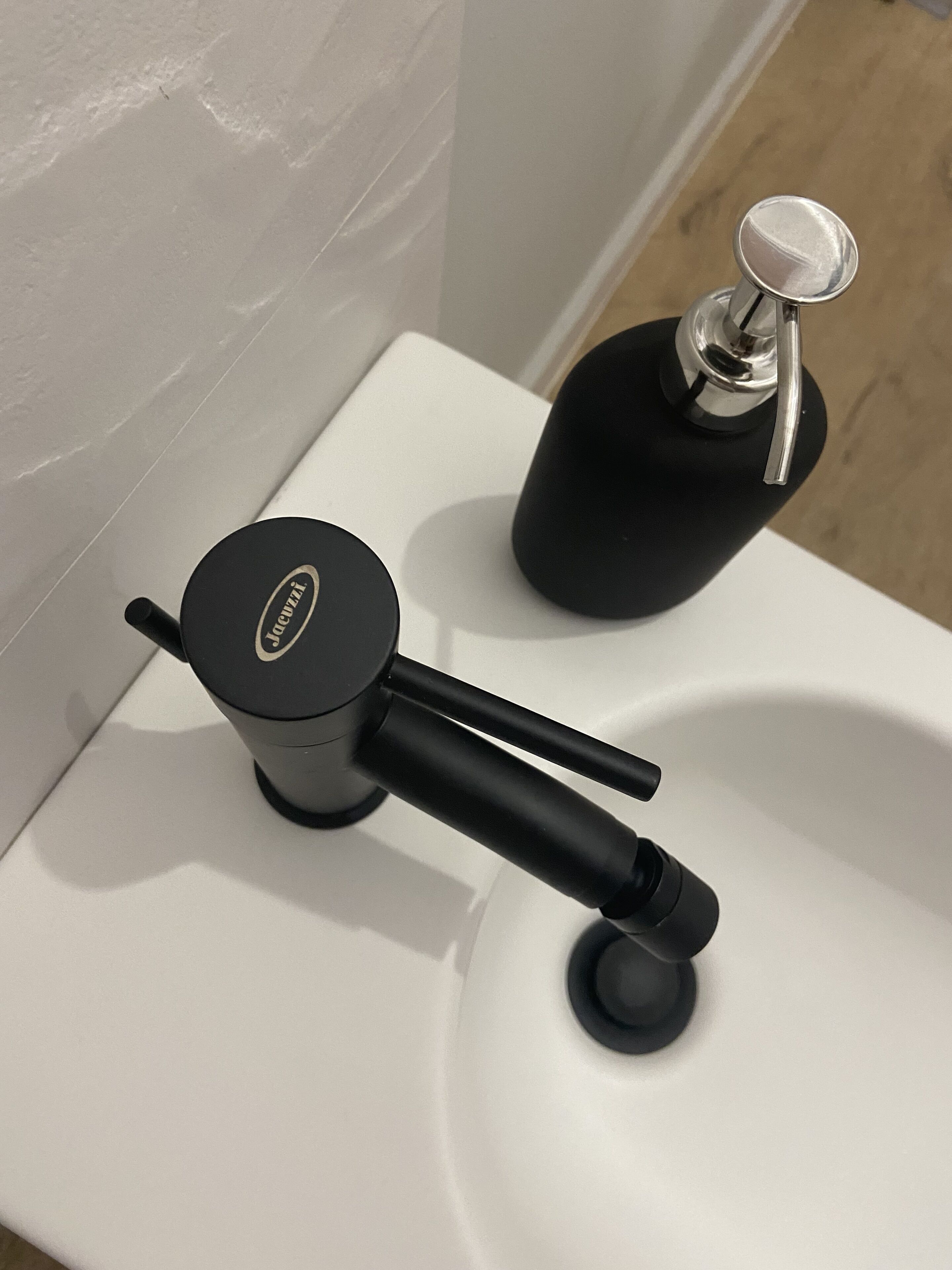 Een moderne wastafel met een zwarte kraan en een fles handzeep.